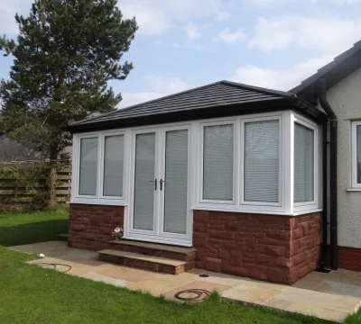 A solid roof conservatory extension with a black slate tiled roof on a sunny day